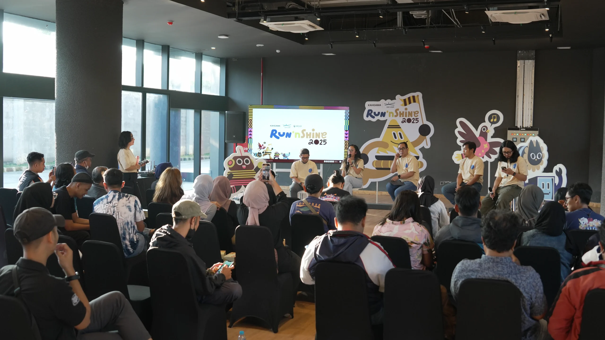 Audiens menghadiri konferensi pers peluncuran Jogja Run’nShine di Gelanggang Inovasi dan Kreativitas Universitas Gadjah Mada, Yogyakarta, dengan layar menampilkan logo acara dan panel pembicara di depan.