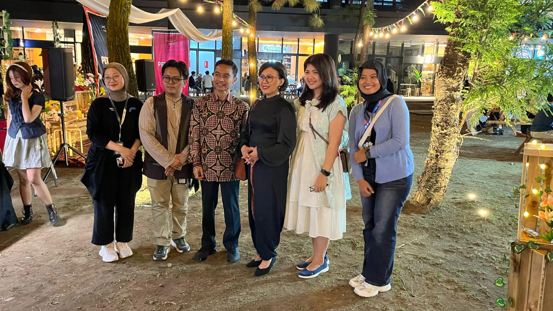 Rektor Universitas Gadjah Mada, Prof. Ova Emilia, berfoto bersama panitia dan peserta di acara Perayaan Jumat Sore GIK UGM yang digelar di Pine Forest, Yogyakarta, dengan latar dekorasi lampu dan booth acara yang meriah.