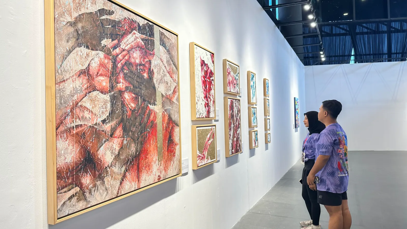 Dua pengunjung berjersey Run'nShine mengamati lukisan di pameran Mampir Gelanggang 2026