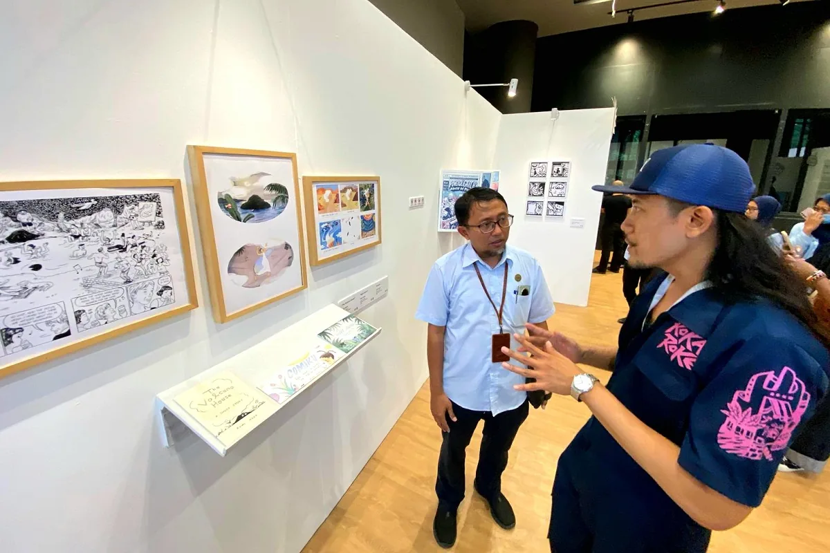 Dua orang berdiskusi di depan karya komik berbingkai pada pameran Yogyakarta Komik Weeks 2026 di GIK UGM